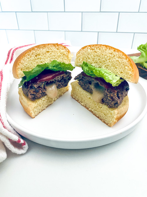 A juicy Lucy burger cut in half on a bun with lettuce.