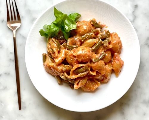 Garlic mozzarella green beans with pasta shells in a white bowl.