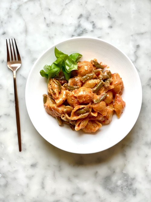 Garlic mozzarella green beans with pasta shells in a white bowl.