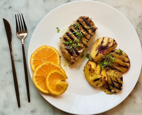 Mustard citrus glazed pork chop with grilled peaches on a white plate.
