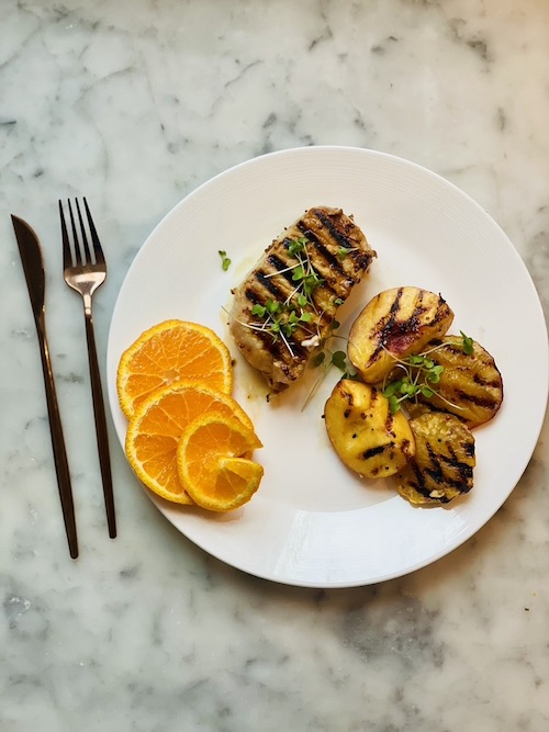 Mustard citrus glazed pork chop with grilled peaches on a white plate.