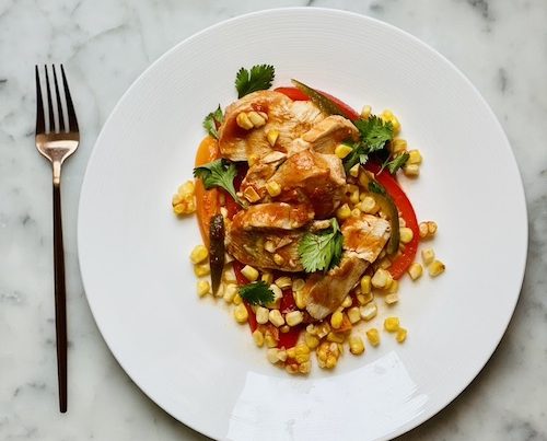 Red Chile chicken with corn and bell peppers on a white dinner plate.