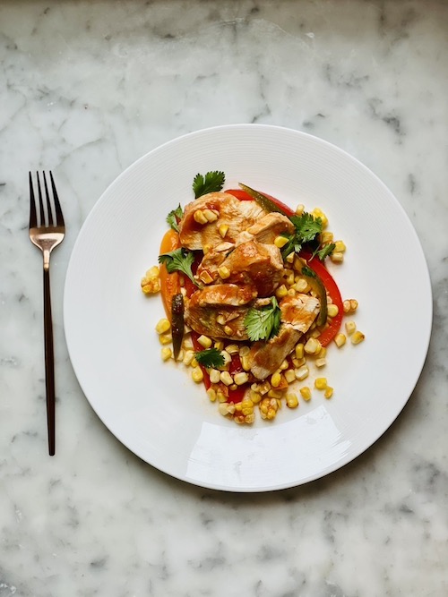 Red Chile chicken with corn and bell peppers on a white dinner plate.