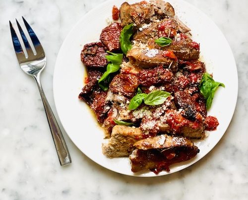Sundried tomato pork chops on a plate with fresh basil.