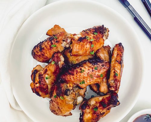 Garlic chili grilled chicken wings on a plate with a set of tongs.