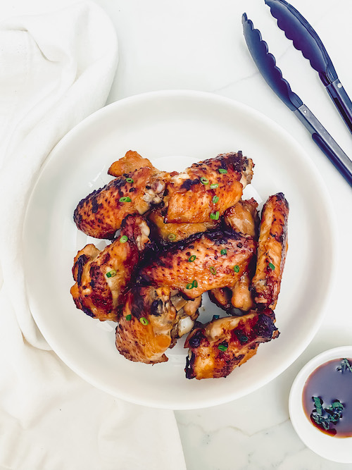 Garlic chili grilled chicken wings on a plate with a set of tongs.