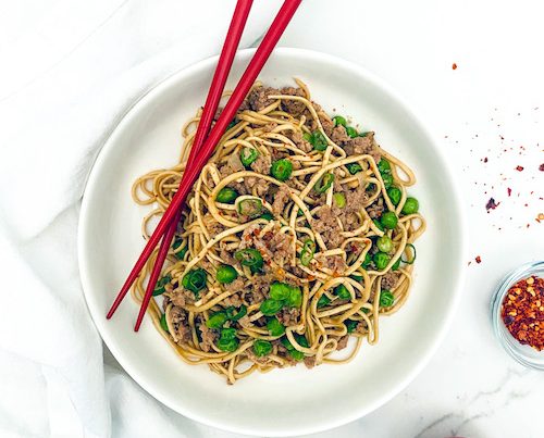 Ground pork and green onions in a bowl of ramen noodles.