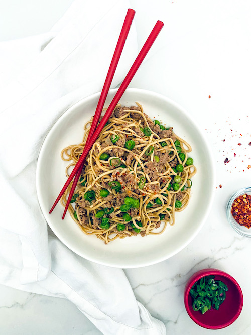 Ground pork and green onions in a bowl of ramen noodles.