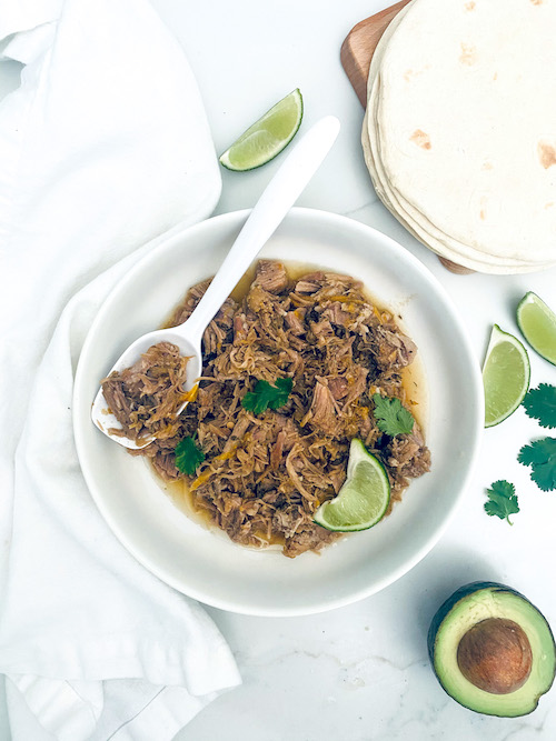Shredded pork fajitas with lime in a white serving bowl with spoon.