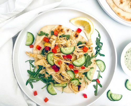 A white dinner plate with shredded chicken shawarma and cucumbers.