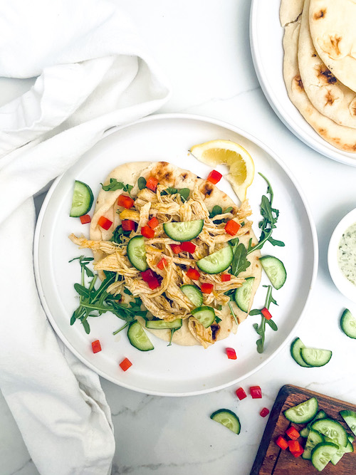 A white dinner plate with shredded chicken shawarma and cucumbers.