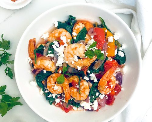 Shrimp with tomatoes and spinach in a white serving bowl.