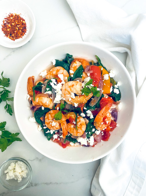 Shrimp with tomatoes and spinach in a white serving bowl.