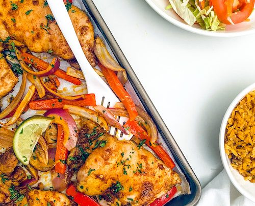 Tandoori chicken thighs with peppers and onions on a sheet pan.