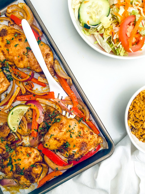 Tandoori chicken thighs with peppers and onions on a sheet pan.