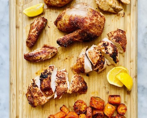 Whole roasted barbecue chicken with carrots on a wooden cutting board.