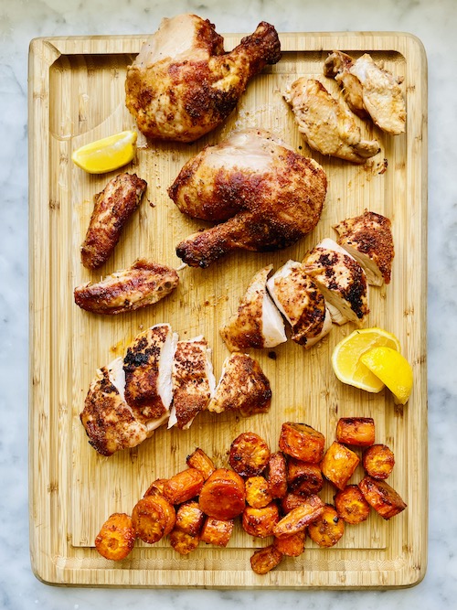 Whole roasted barbecue chicken with carrots on a wooden cutting board.