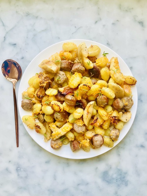 Crispy gnocchi with apples and brats on a white plate.