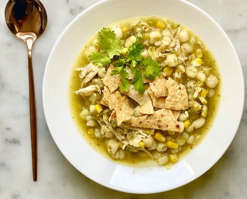Green chicken pozole with hominy in a large white bowl.