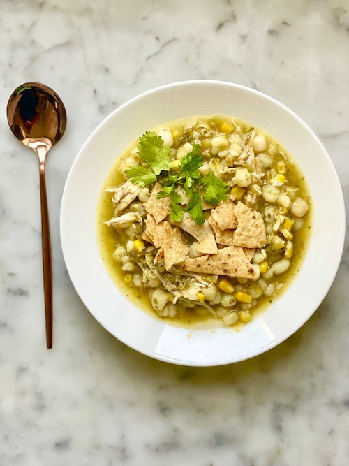 Green chicken pozole with hominy in a large white bowl.