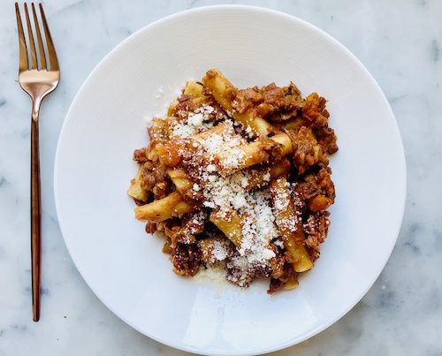 Lentil bolognese over ziti on a white dinner plate.