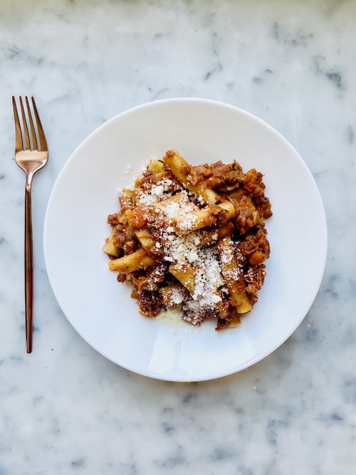 Lentil bolognese over ziti on a white dinner plate.