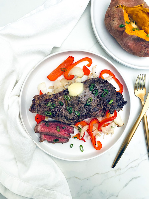 Strip steak that has been air fried resting on a plate with onions and peppers.