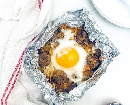 Cheesy hash browns topped with an egg in a foil packet.