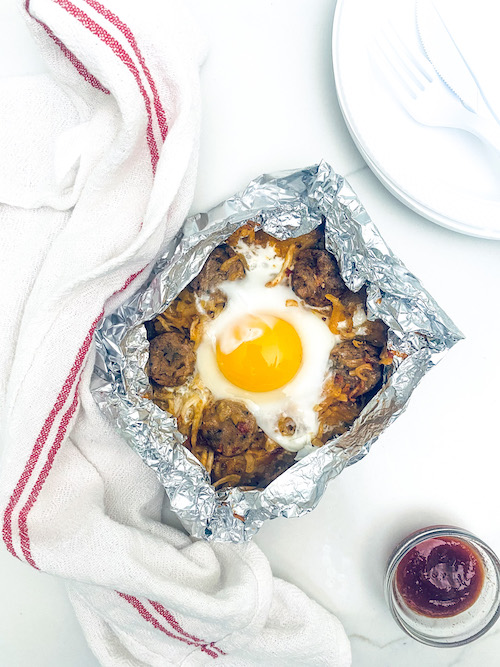 Cheesy hash browns topped with an egg in a foil packet.
