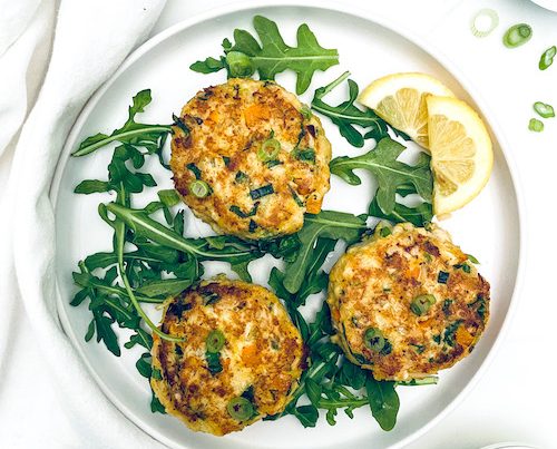 Three crab cakes on a white plate with arugula.