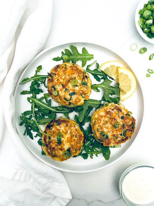 Three crab cakes on a white plate with arugula.