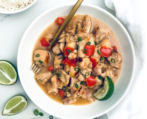 Hawaiian chicken and peppers in a white bowl with lime wedges.