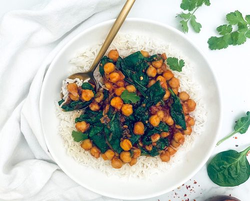 White bowl of rice topped with stewed chickpeas and spinach.