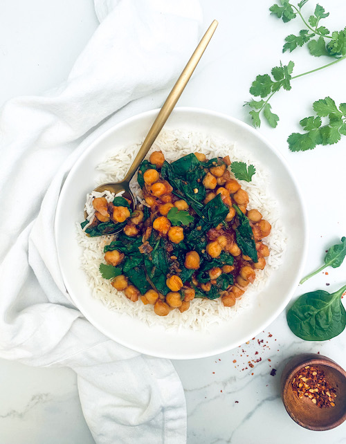 White bowl of rice topped with stewed chickpeas and spinach.
