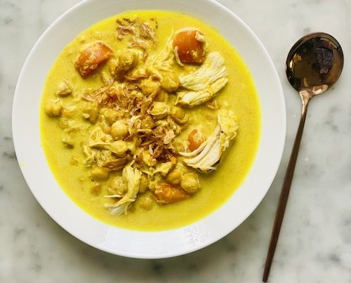 Yellow turmeric ginger coconut chicken in a white bowl.