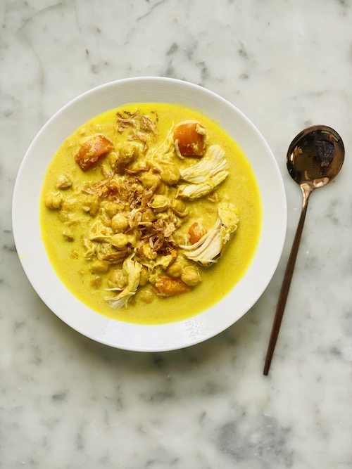 Yellow turmeric ginger coconut chicken in a white bowl.