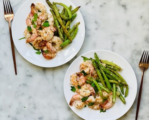 Parmesan crusted shrimp with green beans on white plates.