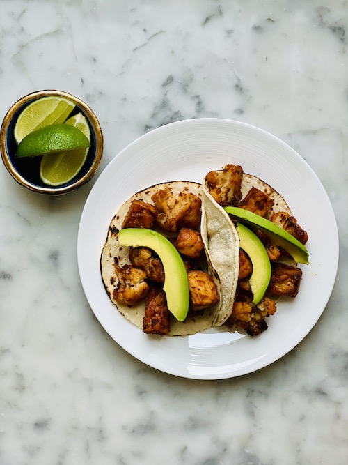 Cauliflower tempeh tacos served with avocado and lime.