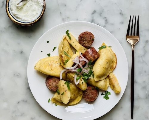 Pierogi and sausage dinner on a white plate.