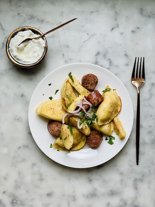 Pierogi and sausage dinner on a white plate.