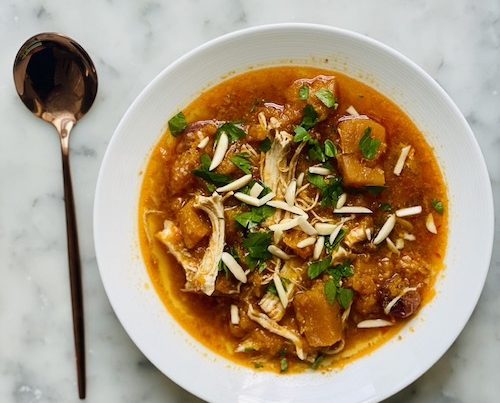 Chicken with butternut squash in broth in a white bowl.