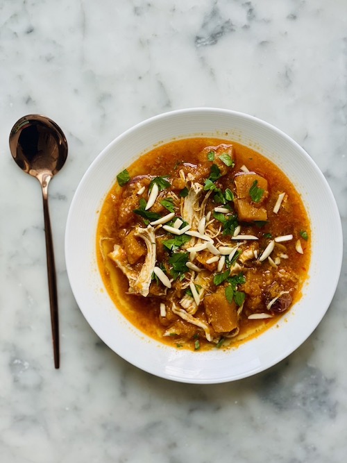 Chicken with butternut squash in broth in a white bowl.