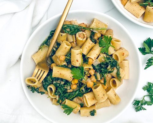 Garlic butter pasta with chickpeas and kale in a large white bowl with a fork.