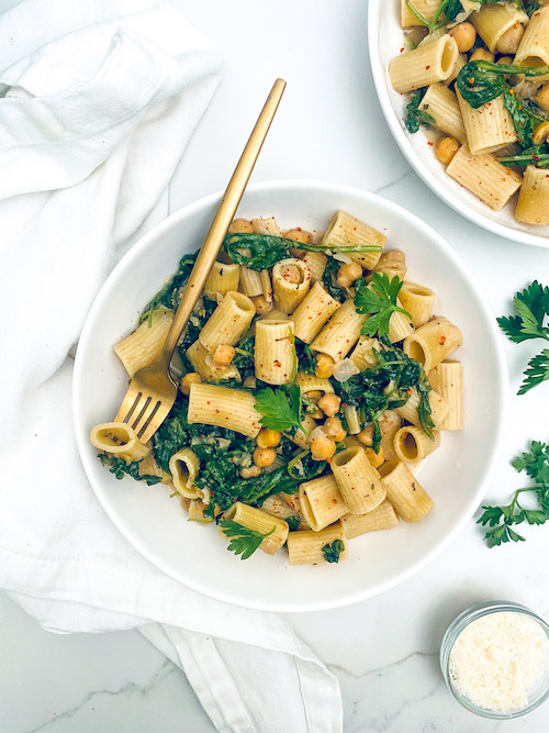 Garlic butter pasta with chickpeas and kale in a large white bowl with a fork.