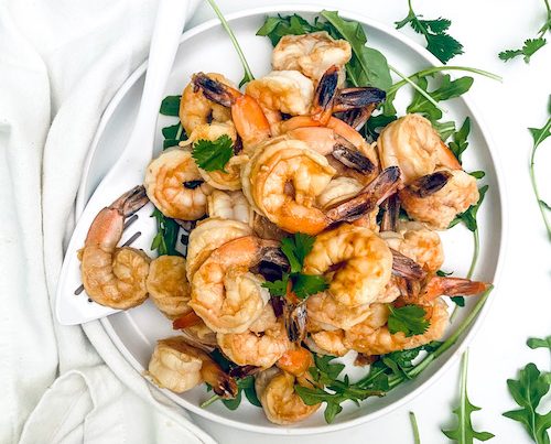 Grilled shrimp piled on a plate with arugula.