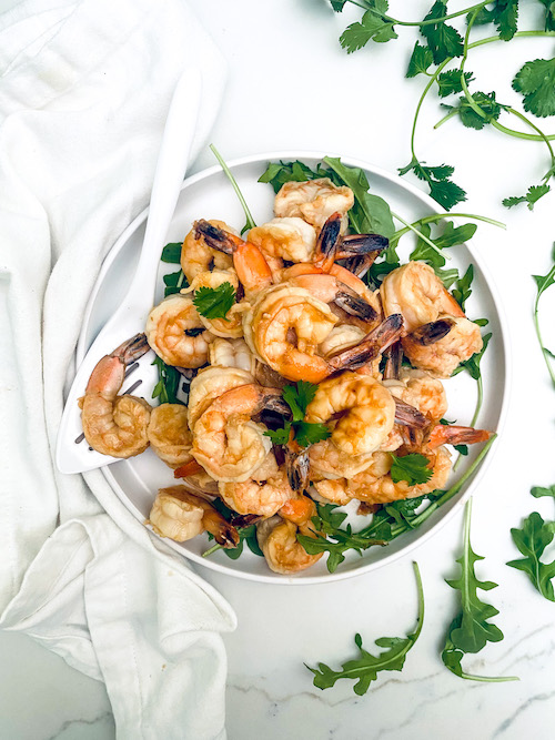 Grilled shrimp piled on a plate with arugula.