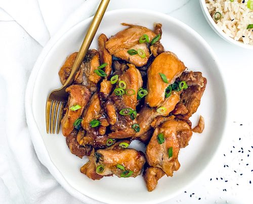 Korean chicken bulgogi on a white plate next to a bowl of rice.
