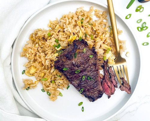 A Korean-style skirt steak on a plate with brown rice and a fork.