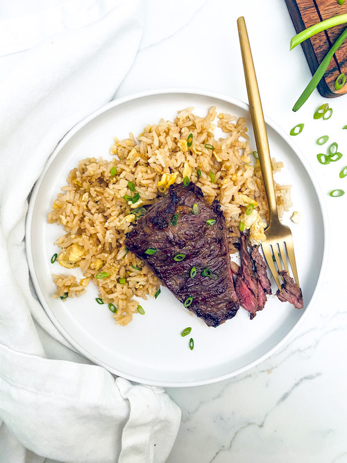 A Korean-style skirt steak on a plate with brown rice and a fork.