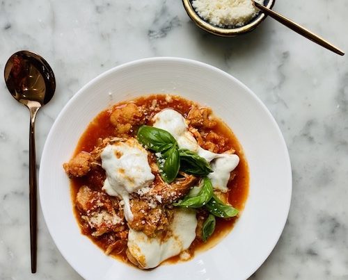 Cauliflower chicken Parmesan in a white bowl with fresh basil.